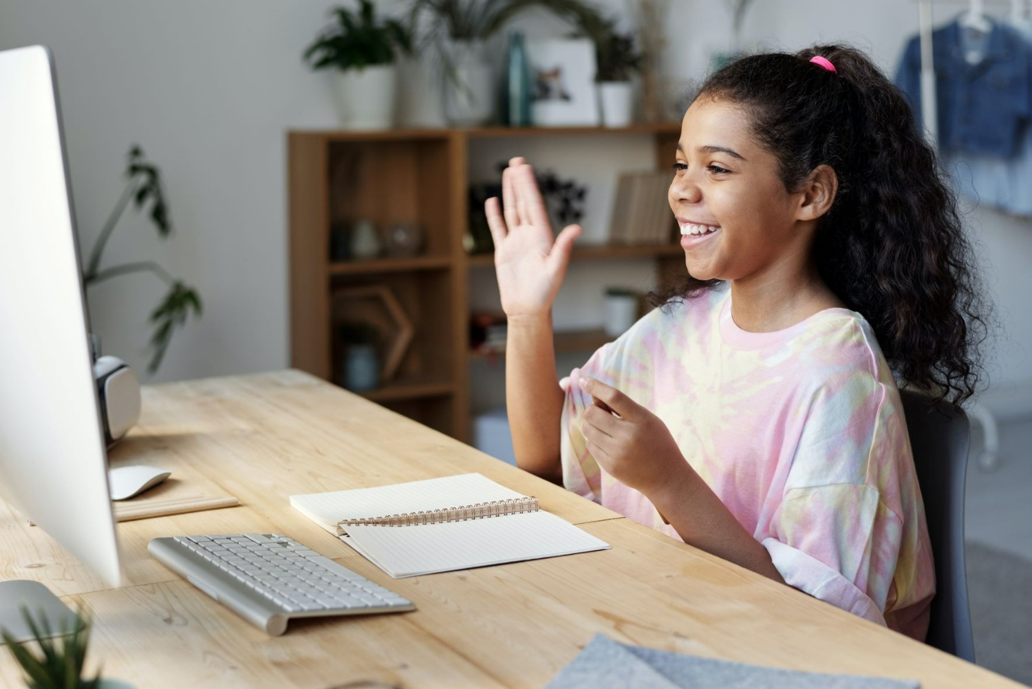 Jeune fille souriante qui participe à un cours en ligne en levant la main droite.
